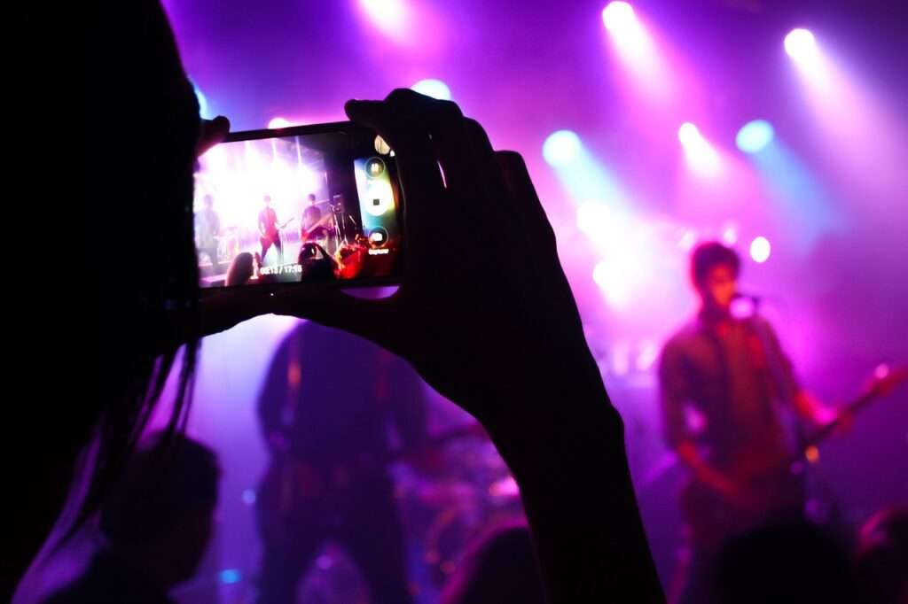 Una persona toma una fotografía con su teléfono celular a un artista que se presenta en el escenario, como parte de las fiestas patronales de una comunidad. 