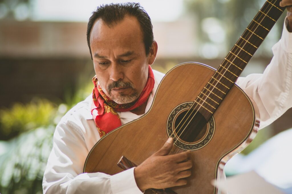 Músico popular, vestido con traje regional, toca una guitarra, como parte de su presentación en un evento de fiestas patrias en México. 