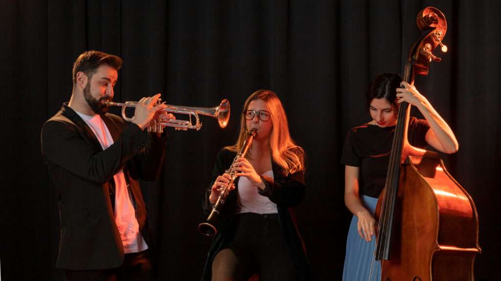 Ensamble musical compuesto por dos mujeres y un hombre se presentan en un escenario, como parte de la contratación legal de artistas.